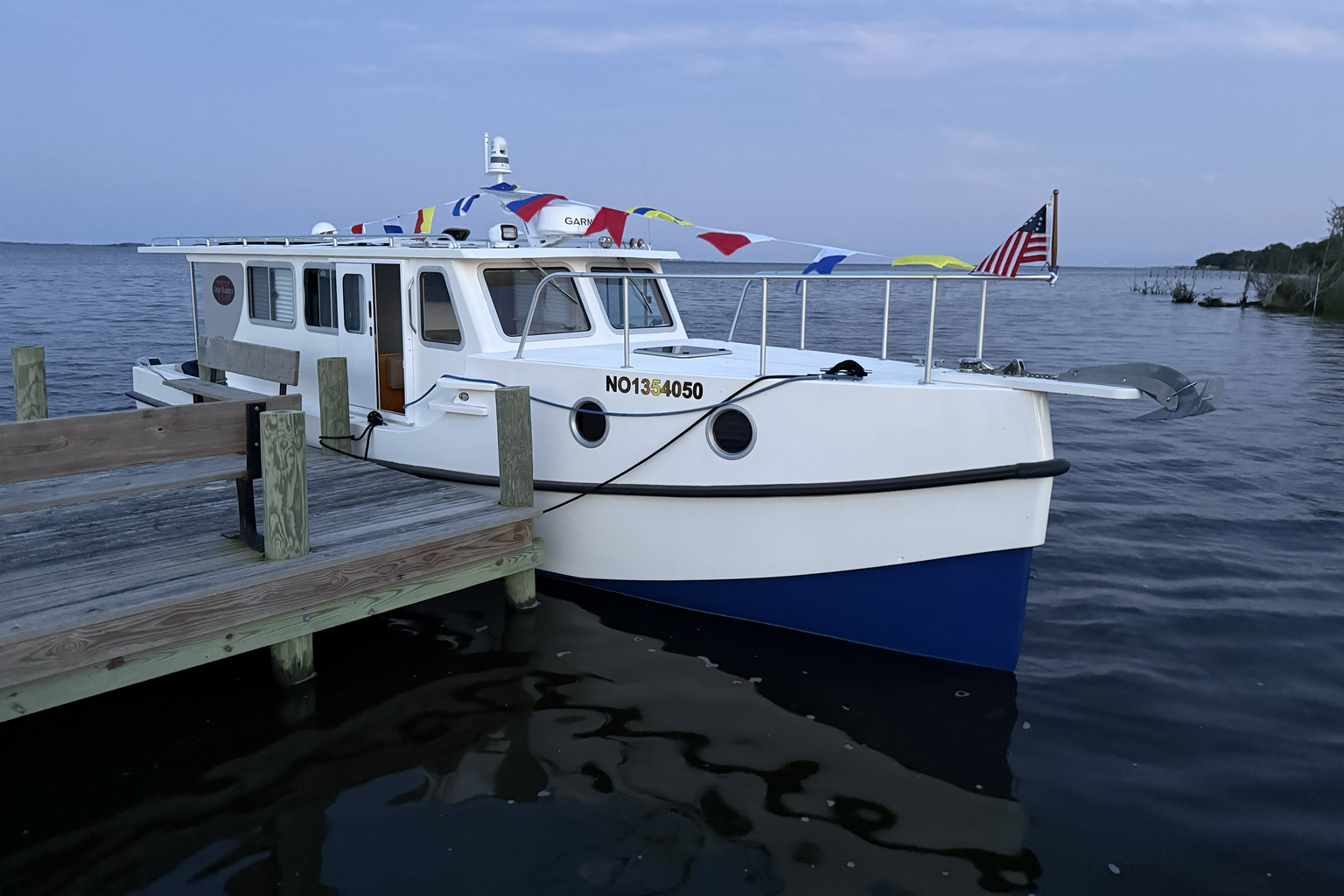 Ulysses tied at a quiet soundside dock with the bow, cabin, blue hull, and rail visible.
