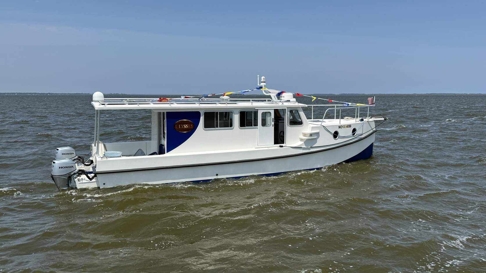 Side profile of Ulysses, a white-and-blue Great Harbour TT35 shallow-draft trawler, cruising on Currituck Sound water.